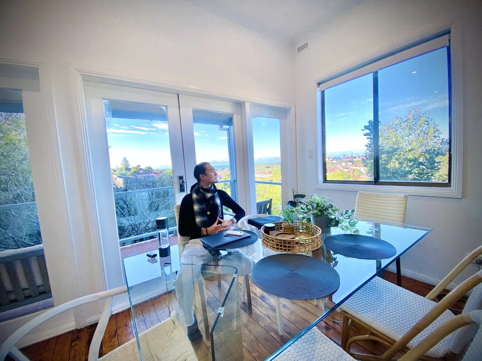 Freeman Fung working at a glass table beside tall windows overlooking a wooded valley