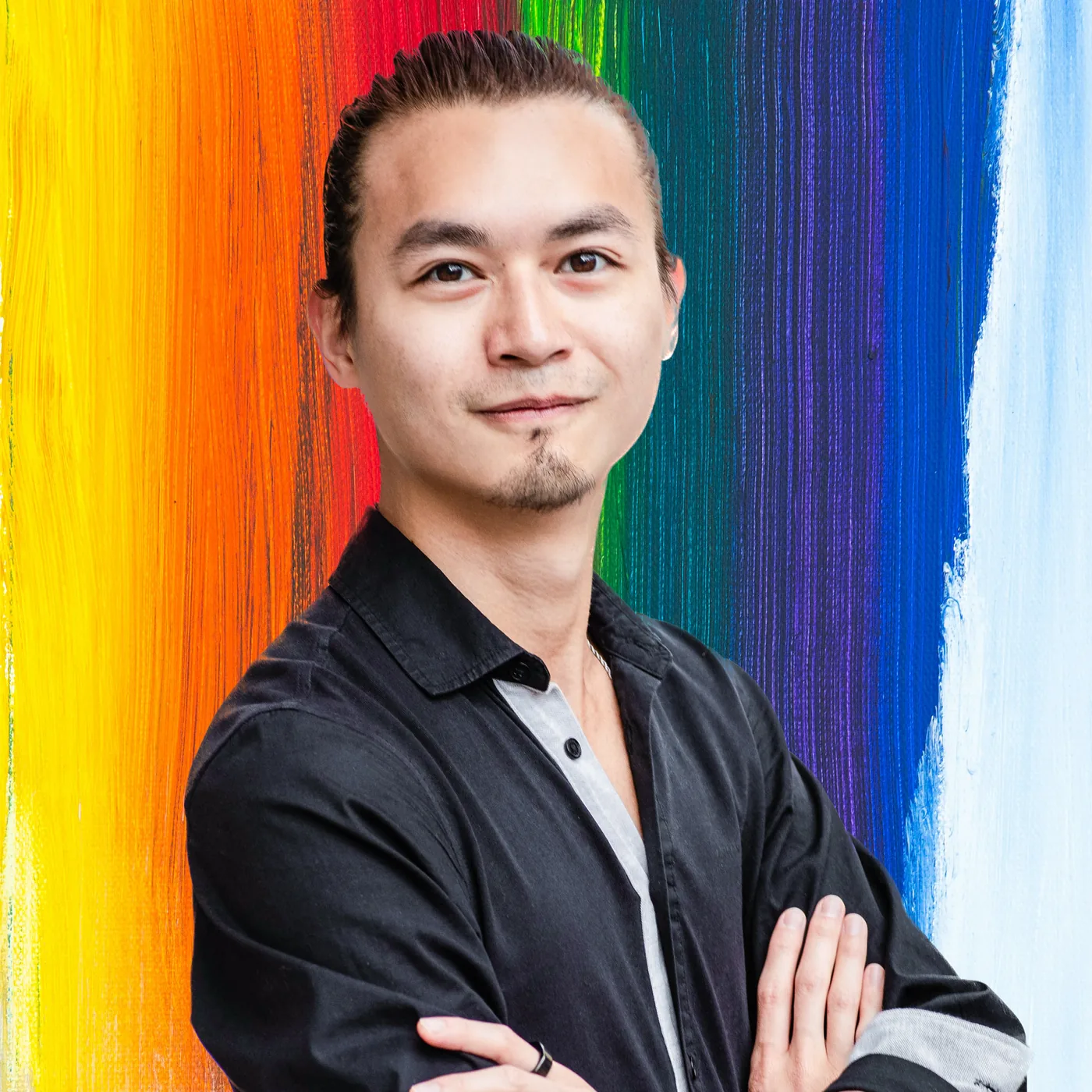 Freeman Fung with arms folded, in front of a brightly painted rainbow wall