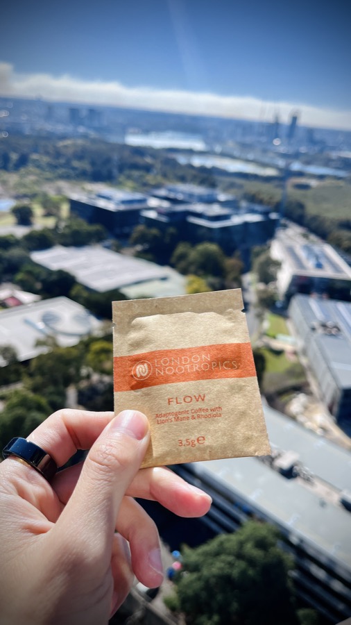 London Nootropics FLOW adaptogenic coffee sachet held up with a city view behind