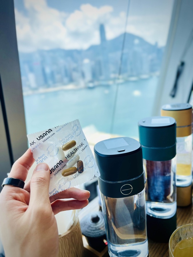 USANA HealthPak sachet held up against the Hong Kong harbour skyline